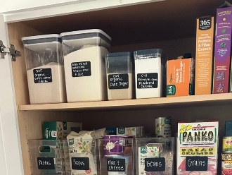 A pantry cabinet with clear canisters and bins, each with a chalkboard label for pasta, beans, grains and sugar