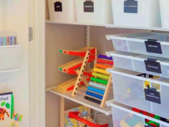A playroom closet with white labelled bins, clear toy drawers and a wooden abacus